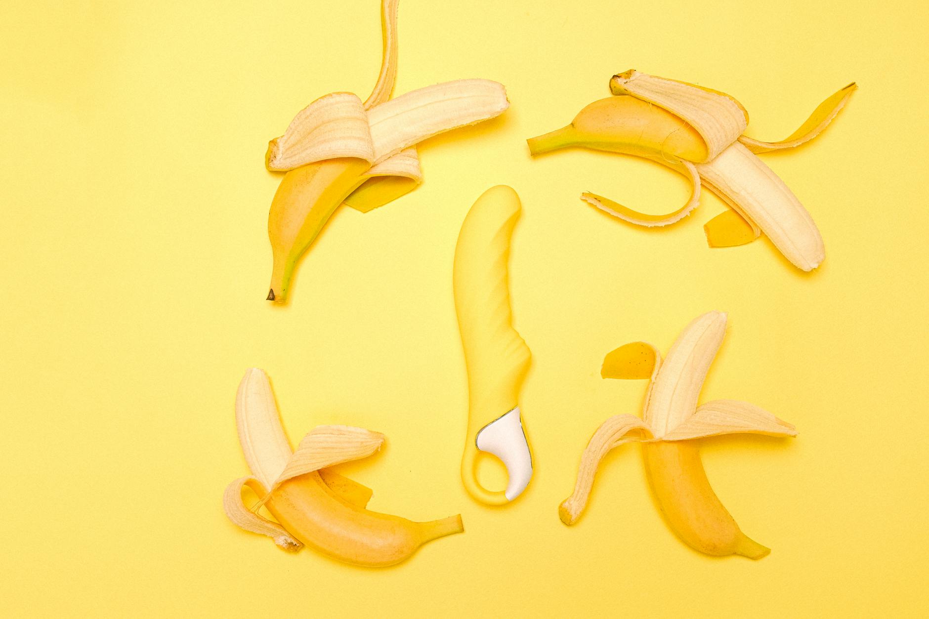 Vibromasseur citron jaune en silicone entouré de bananes pelées sur un fond jaune vif