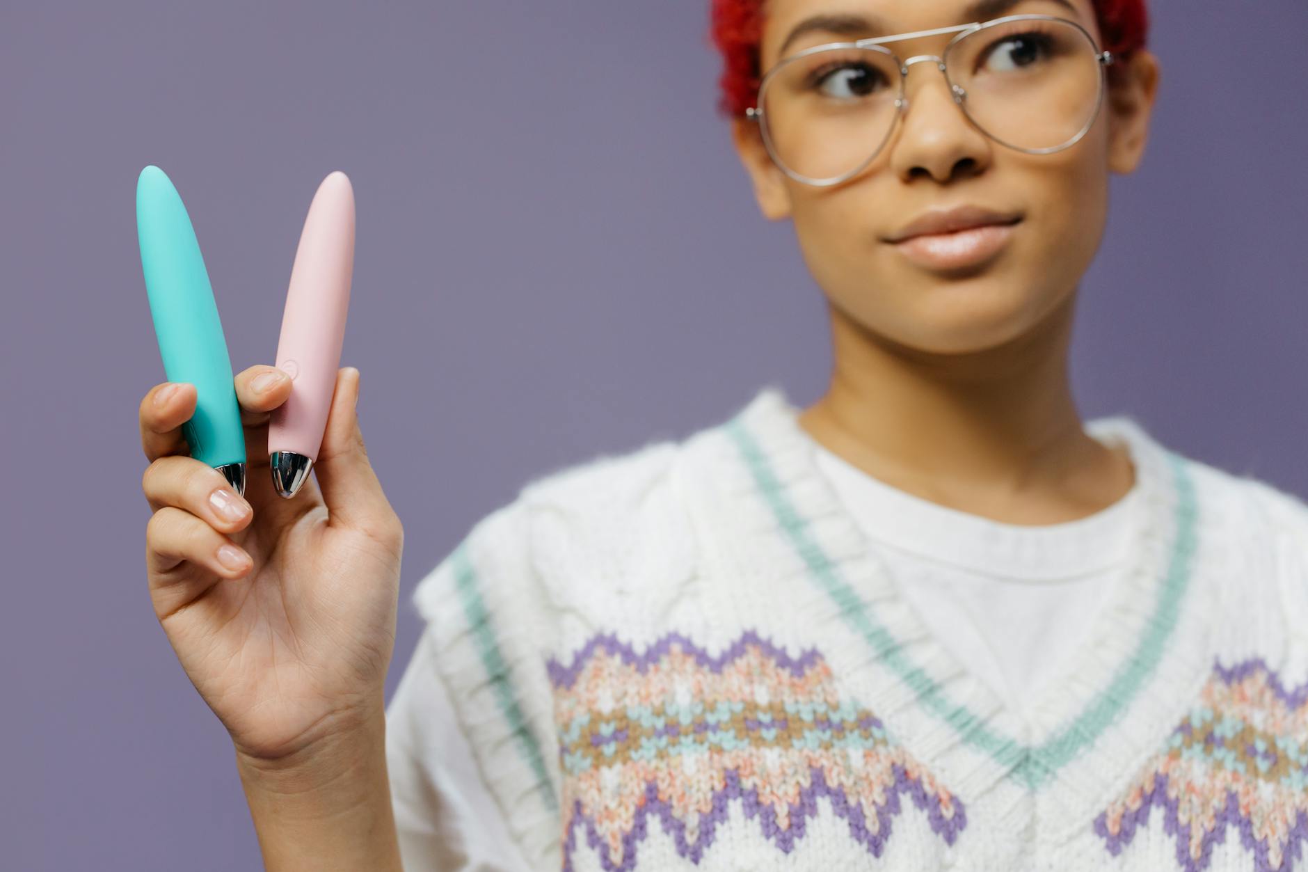 A woman holding colorful clitoral vibrators including lemon vibrators against a purple background