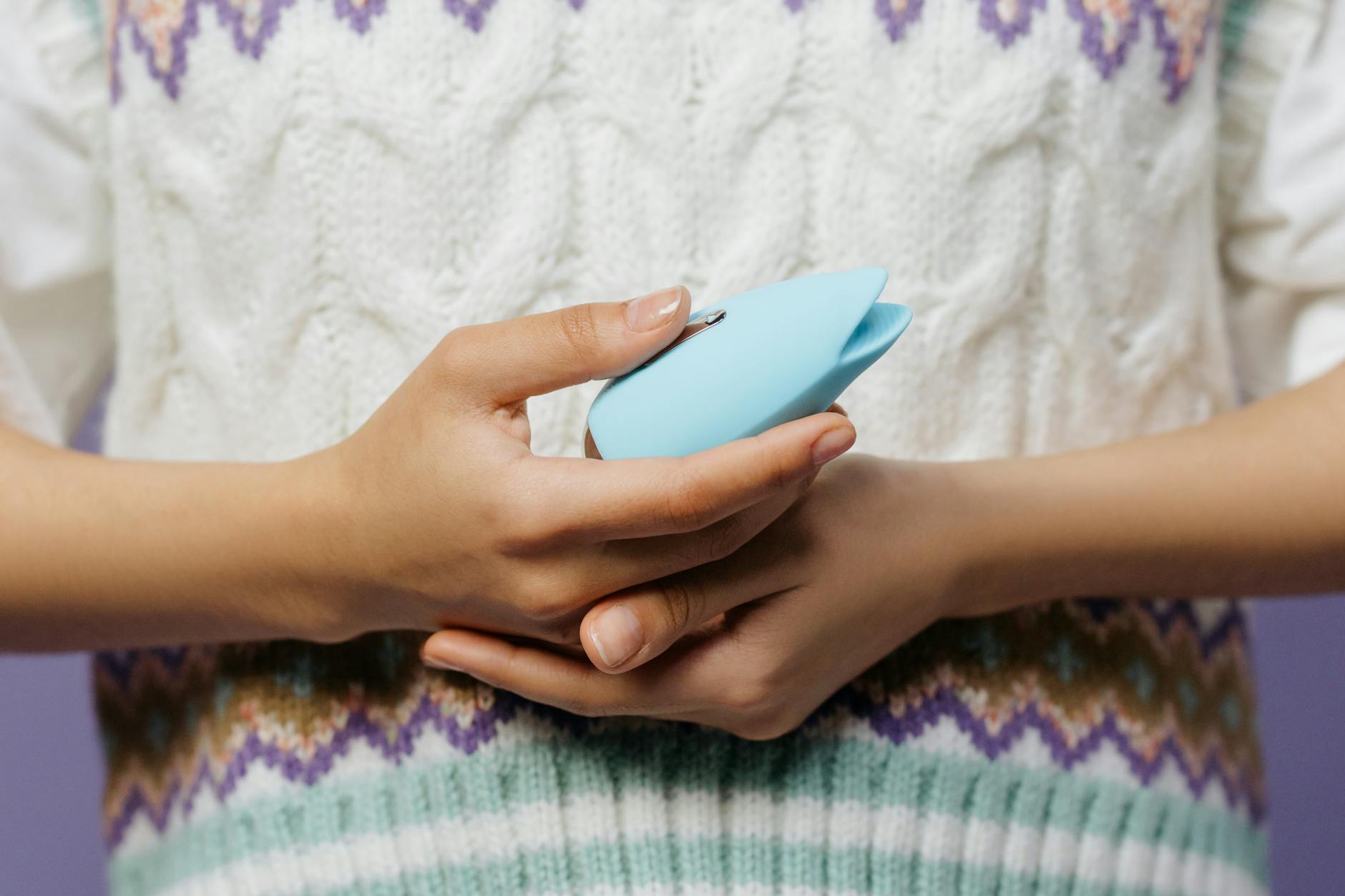 Gros plan des mains tenant un vibromasseur bleu contre un pull tricoté.