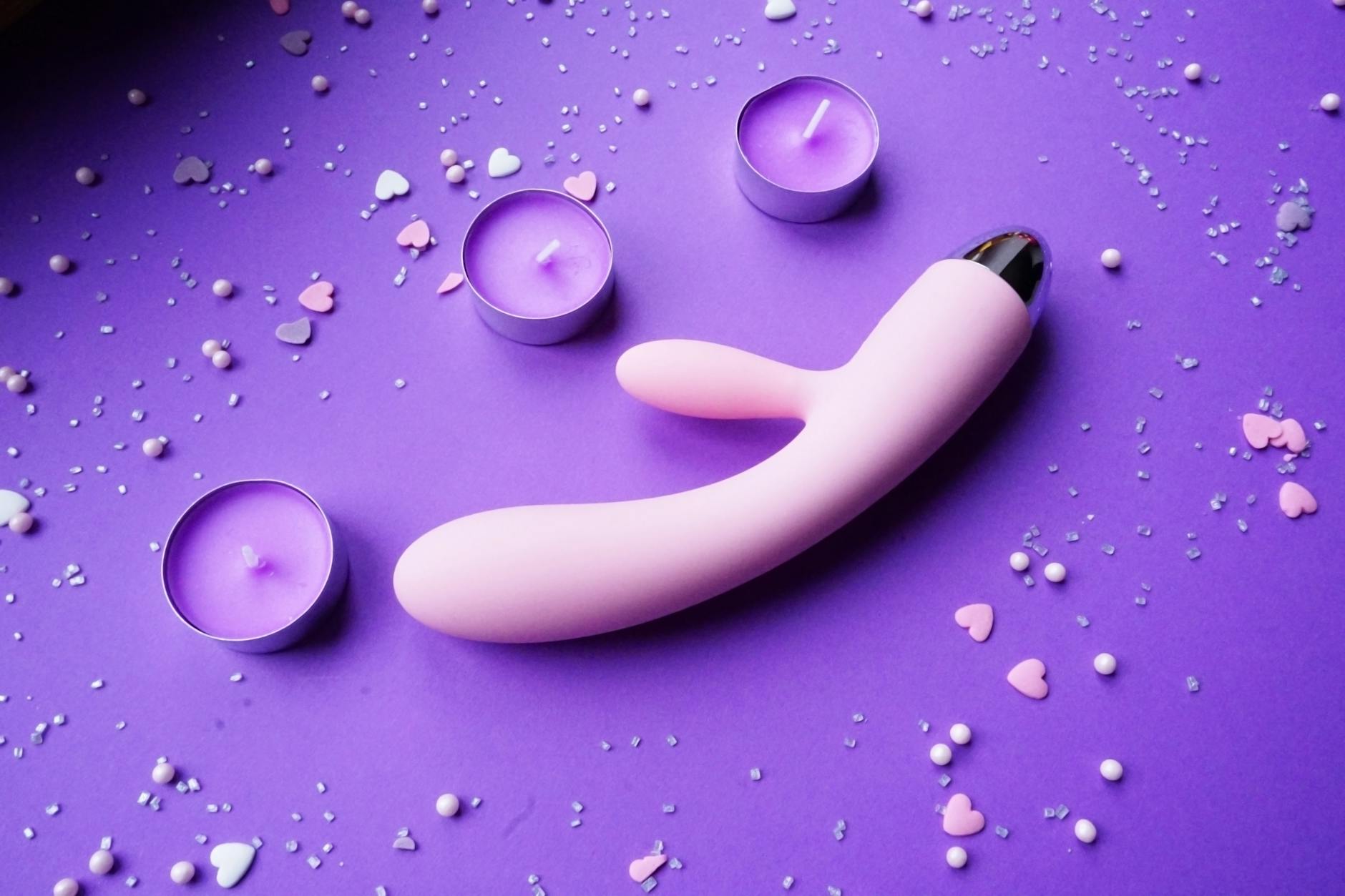 Vibromasseur rose sur fond violet avec confettis en forme de cœur et bougies pour créer une ambiance romantique